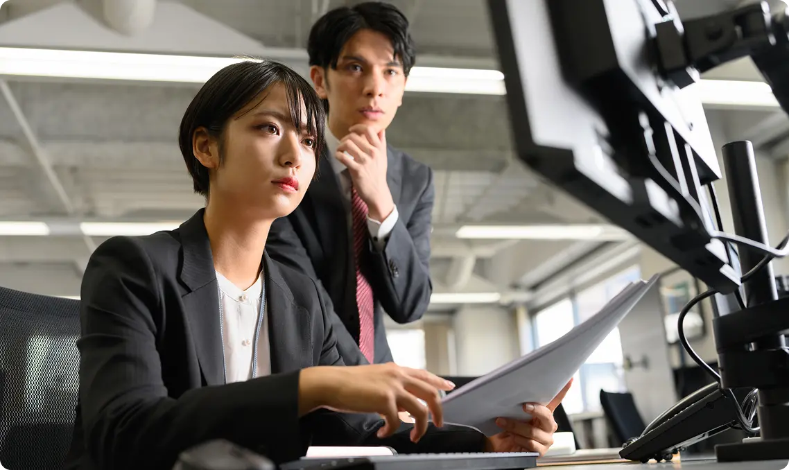 スーツを着た若い男女がオフィスでパソコン画面を真剣に見つめている